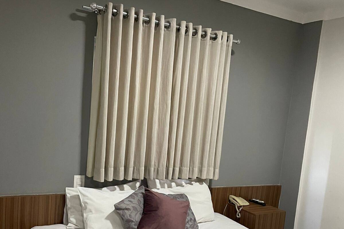 A hotel room with a bed, a telephone, a towel, and a curtain.