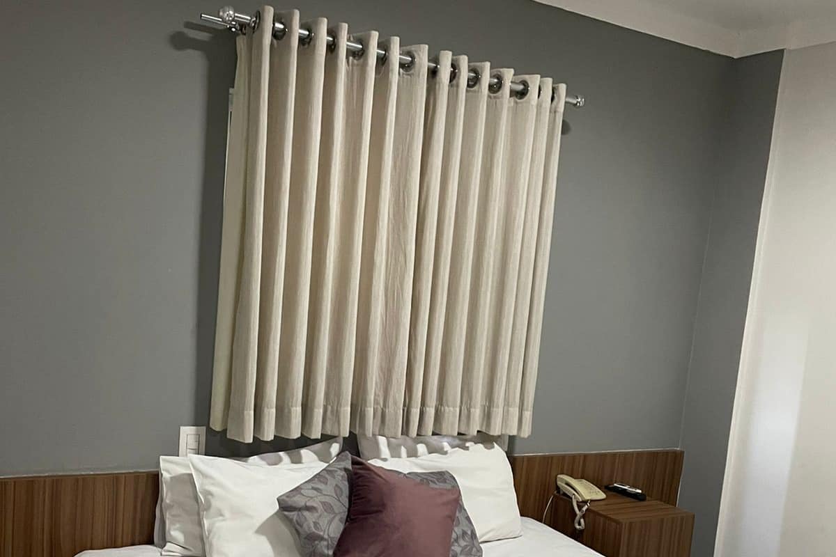 A hotel room with a bed, pillows, a telephone, and a curtain.