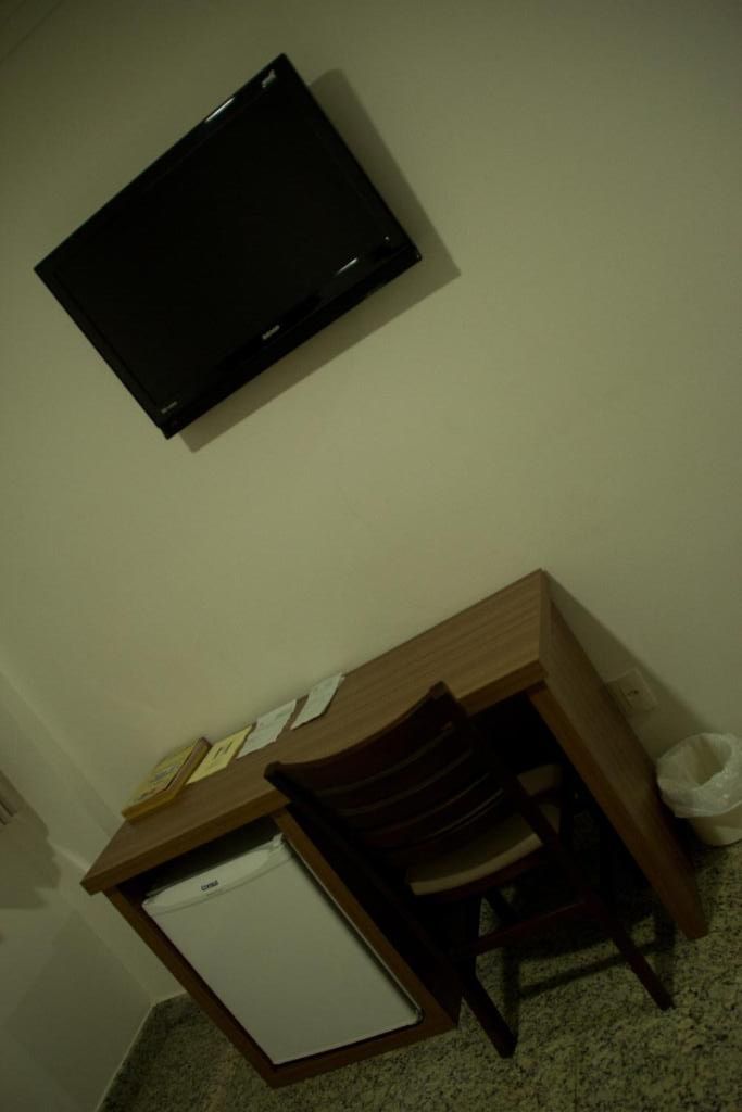 A small room with a desk, chair, and a television mounted on the wall.