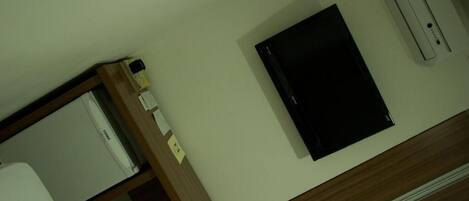 Une chambre d’hôtel équipée d’un lit, d’un bureau, d’une petite table et d’un téléviseur fixé au mur.