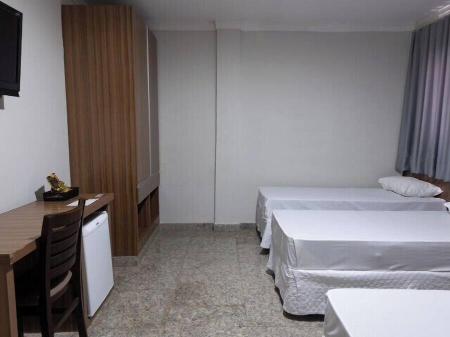 A hotel room with a wooden desk, a television, two beds, and a small kitchenette.