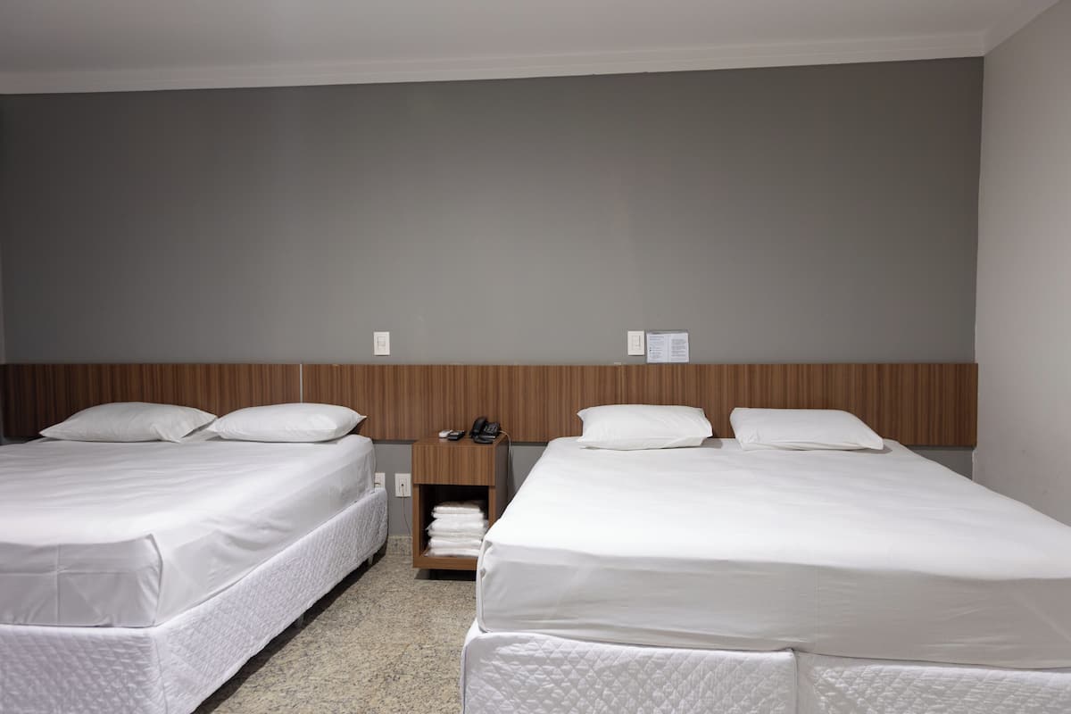 A hotel room with two beds, a wooden headboard, a bedside table with a phone, and a wall-mounted light switch.