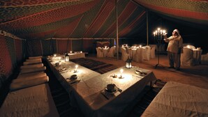 Un área de comedor con carpas, mesas dispuestas para una comida, velas y una persona de pie junto a un candelabro.