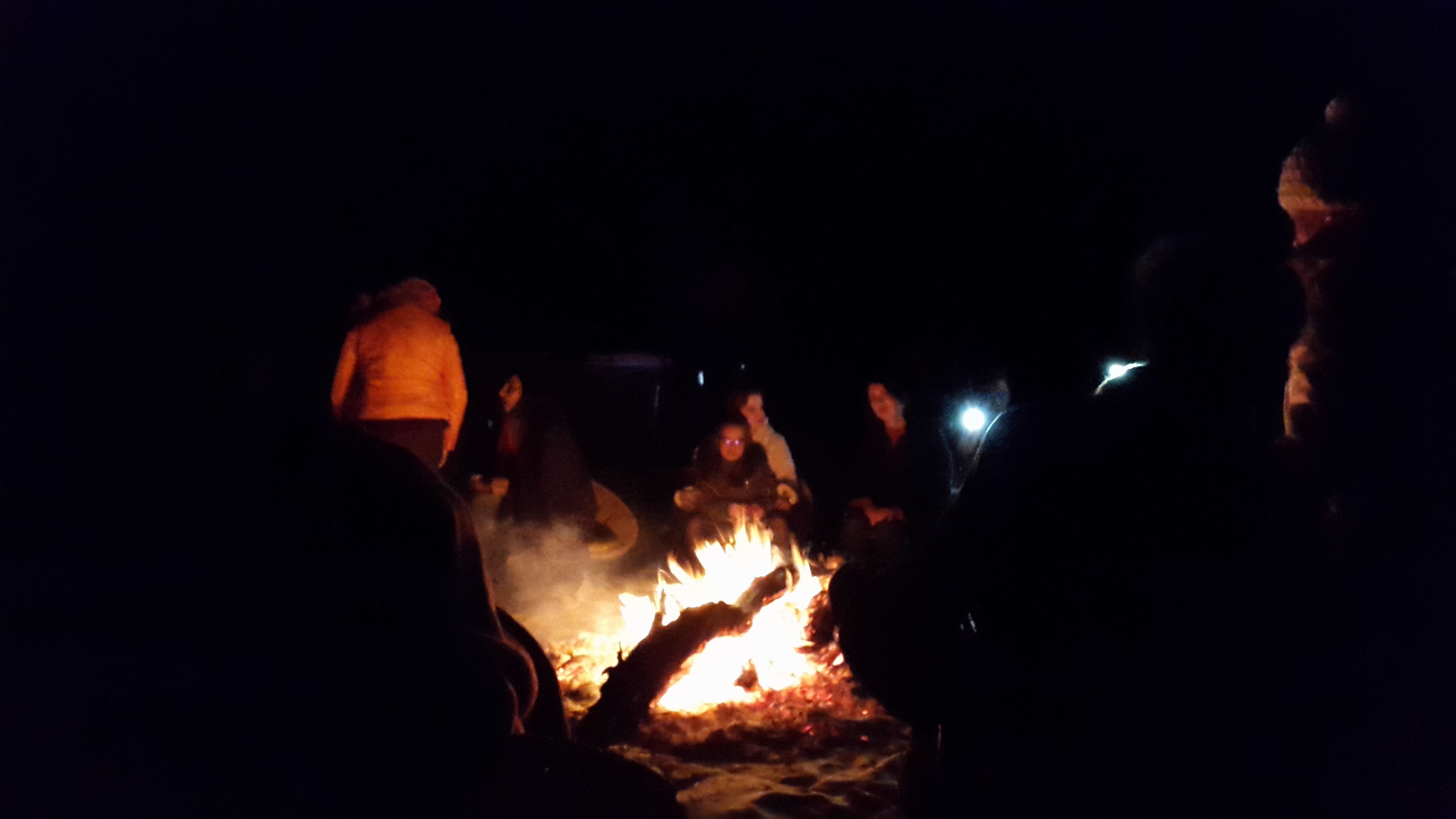 Un grupo de personas reunido alrededor de una fogata por la noche.