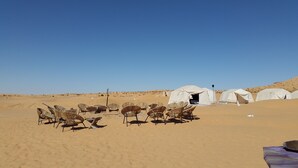 Campaamento en el desierto con tiendas blancas y sillas de mimbre dispuestas para los huéspedes.