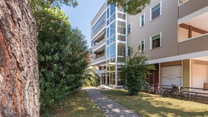 Un edifici d'apartaments modern amb un camí de pedra, vegetació i bicicletes.
