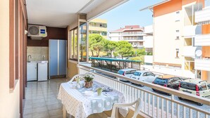 Un balcó amb taula preparada per dinar, nevera i finestra amb vista a un carrer amb cotxes estacionats i edificis.