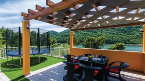 Une terrasse couverte avec un trampoline, des sièges d’extérieur et une vue magnifique sur un lac et une forêt.