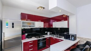 Une cuisine moderne avec des meubles de rangement rouges et blancs, des appareils électroménagers en acier inoxydable et un four encastré.