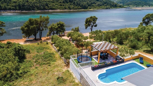 Un espace aménagé au bord de la piscine, avec un trampoline, des sièges et une vue sur un lac et des montagnes.