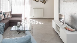Una sala moderna con un sofá seccional, una mesa de centro de vidrio, un mueble blanco para entretenimiento y una pieza decorativa en la pared.