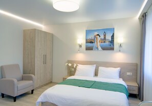 A hotel room with a bed, a chair, a wardrobe, and a painting on the wall. - Arena Summit Apart Hotel (Kyiv)