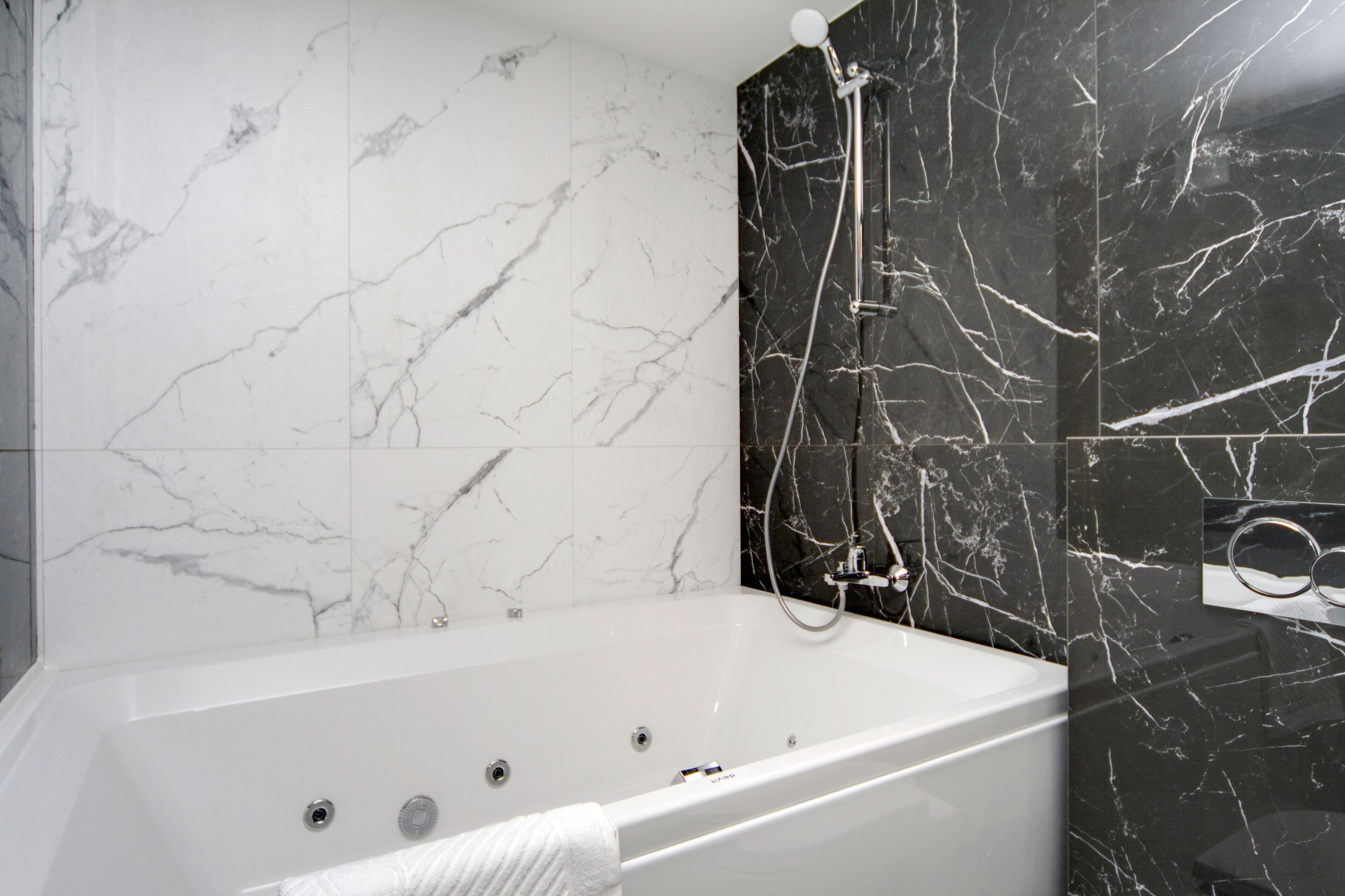 A modern bathroom with a marble wall, a white bathtub, and a showerhead.