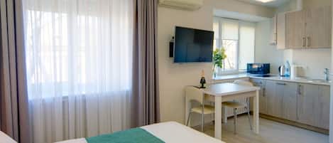 A hotel room with a bed, a desk, a chair, a TV, and a kitchenette.