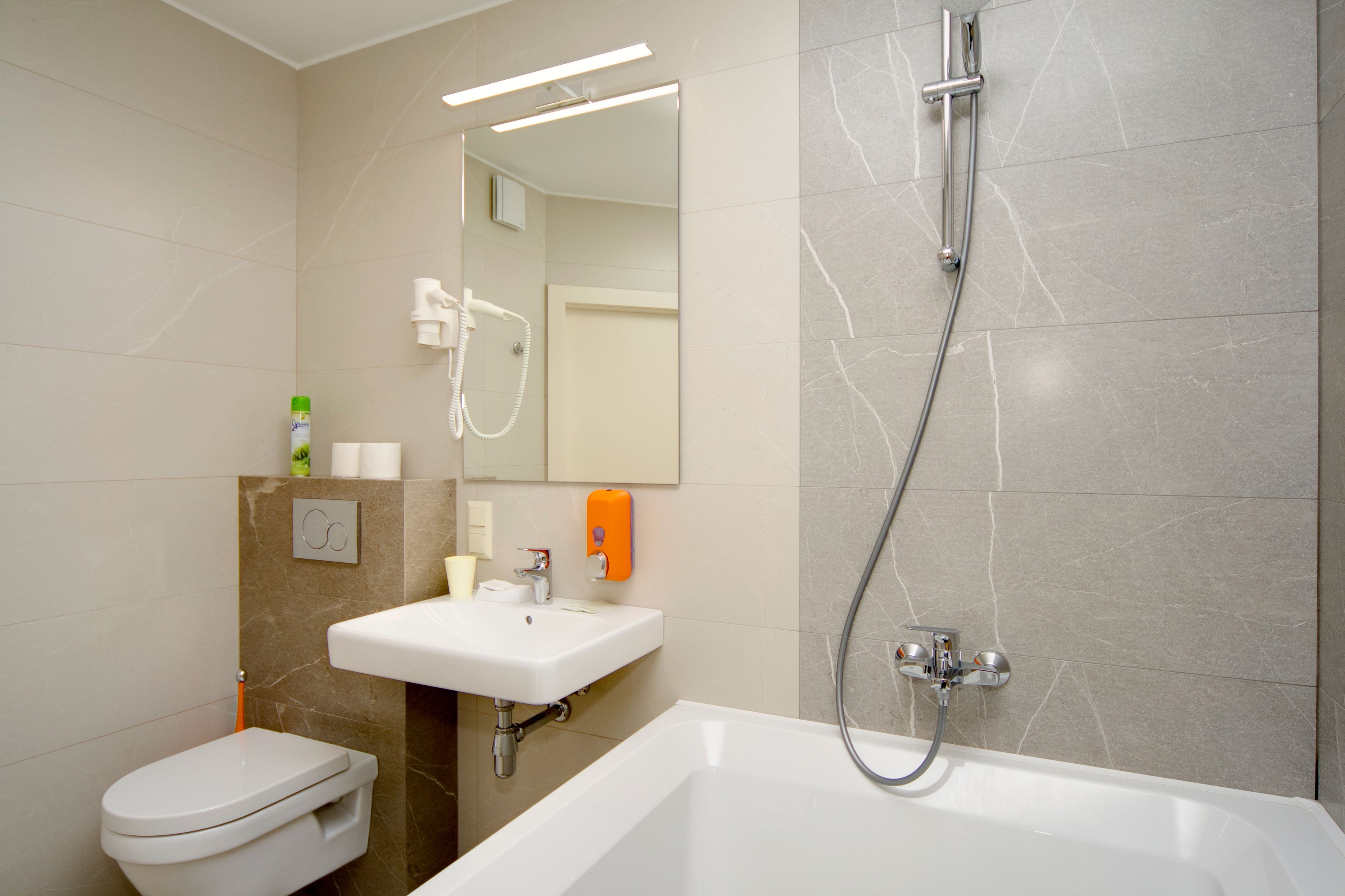 A modern bathroom with a toilet, sink, mirror, and bathtub.