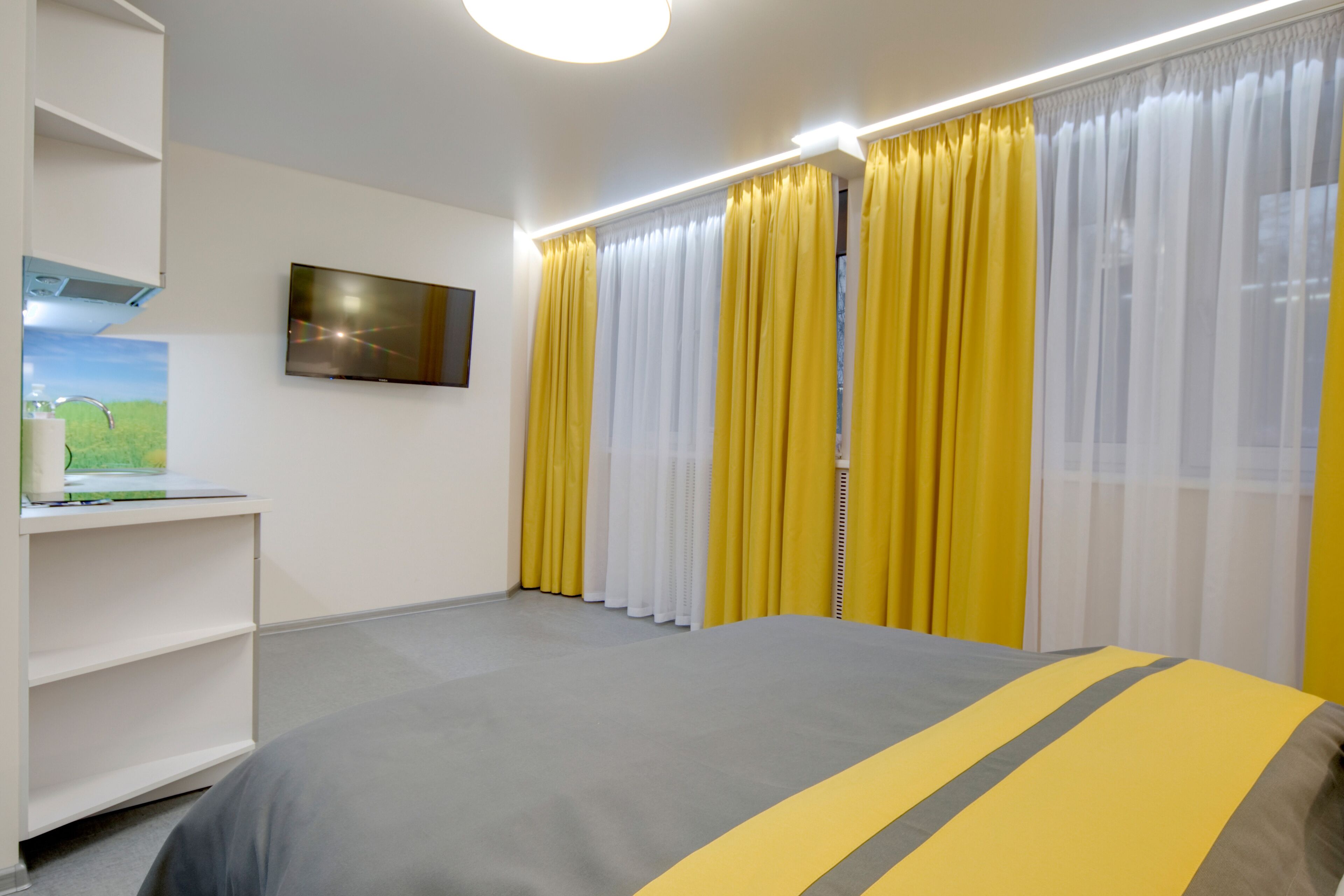 Quarto de hotel com cama, televisão, estante com um laptop e cortinas.