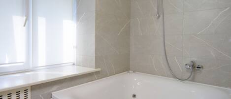 A bathroom with a white bathtub, a shower, and a window.