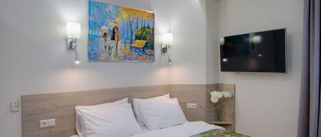 Una habitación de hotel con una cama, un cuadro, un televisor y una mesita de noche con una lámpara.