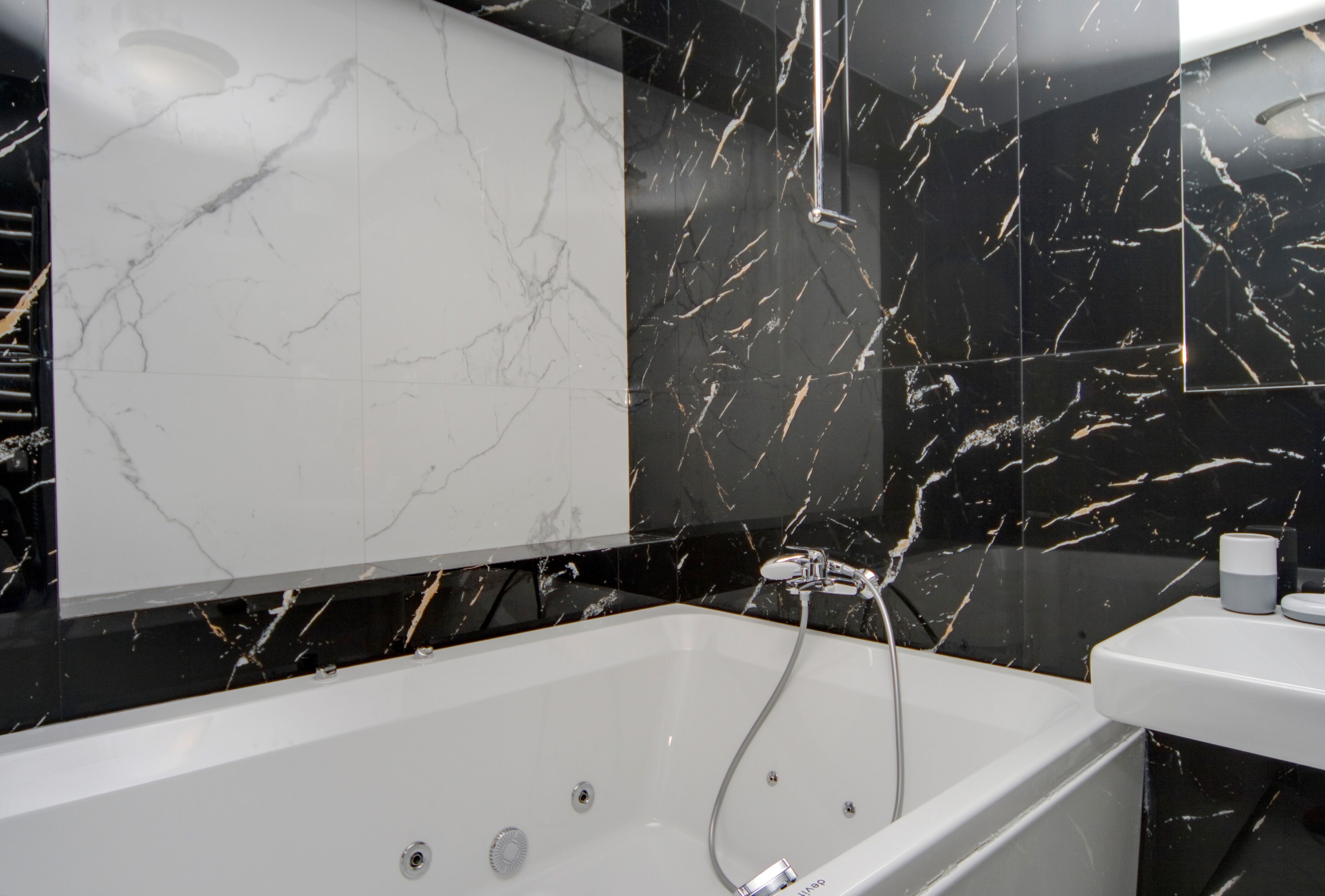 A modern bathroom with a white bathtub, black marble walls, and a large mirror.
