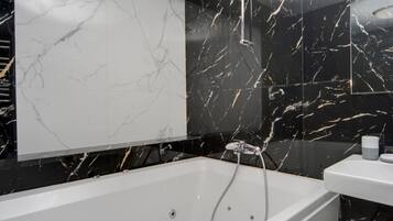 A modern bathroom with a white bathtub, black marble walls, and a large mirror.