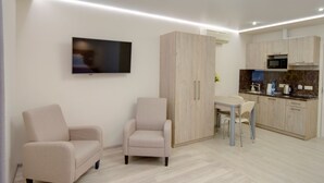 A modern, compact living space with a sofa, armchair, dining table, and kitchen area.
