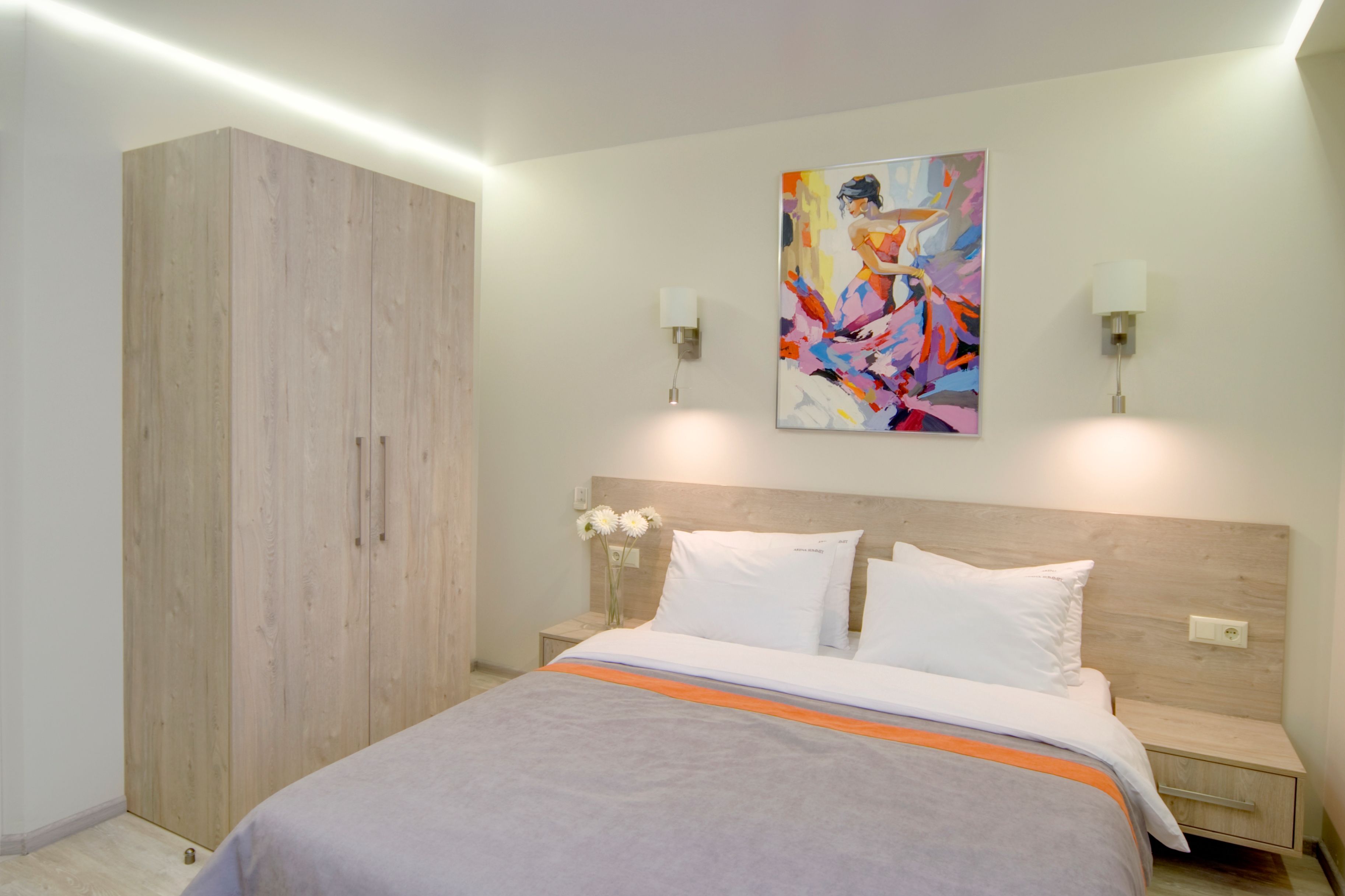 Ein modernes Schlafzimmer mit einem großen Bett, einem Holzschrank und einem farbenfrohen, abstrakten Gemälde an der Wand.