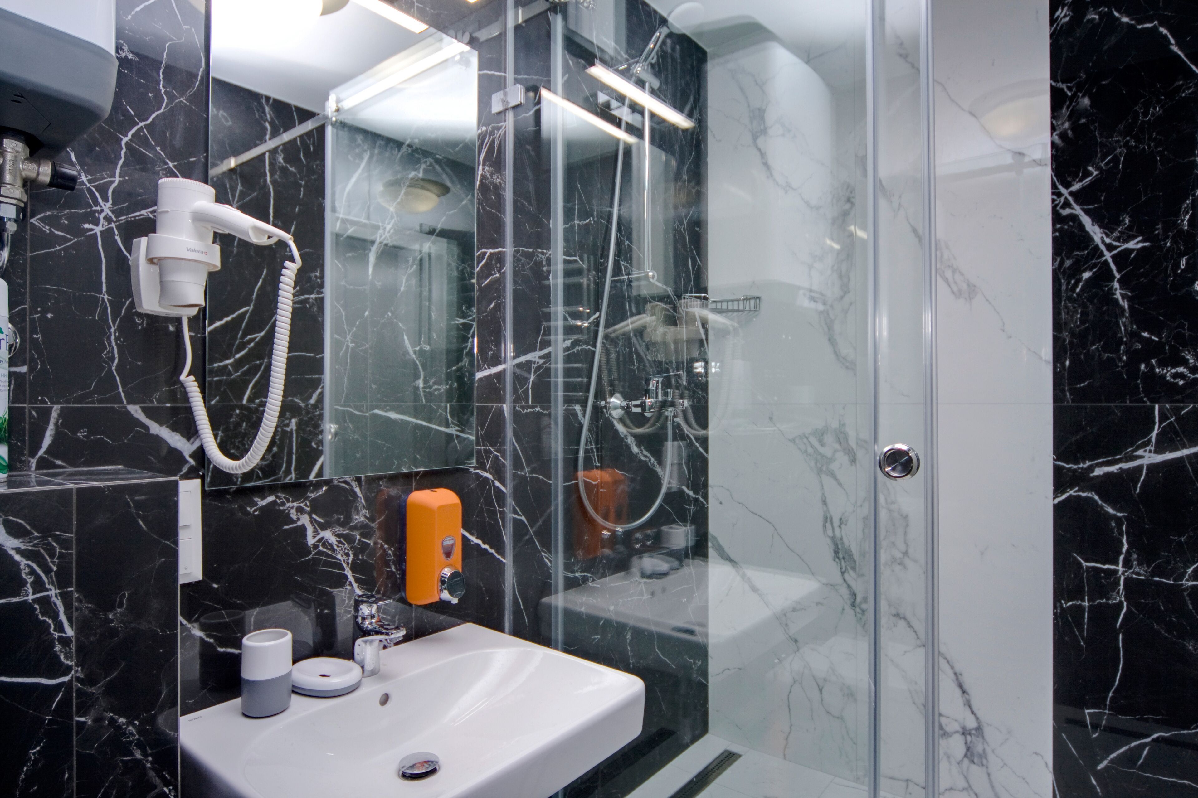 A modern bathroom with a glass shower enclosure, a white sink, and a hairdryer mounted on the wall.