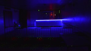 A dimly lit room with a blue-lit bar area and a visible door. - Peace & Grace Motel (Kigali)