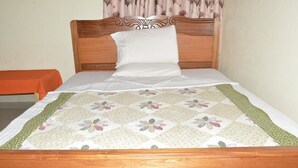 A neatly made bed with a floral quilt, a wooden headboard, and a plain wall with a curtain. - Peace & Grace Motel (Kigali)