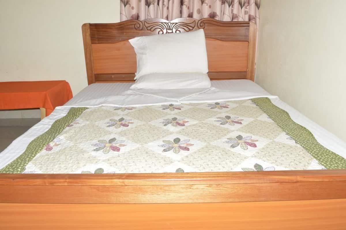 A neatly made bed with a floral quilt, a wooden headboard, and a plain wall with a curtain.