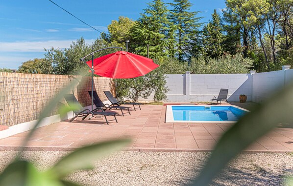 En trädgård med en pool, solstolar och ett rött parasoll.