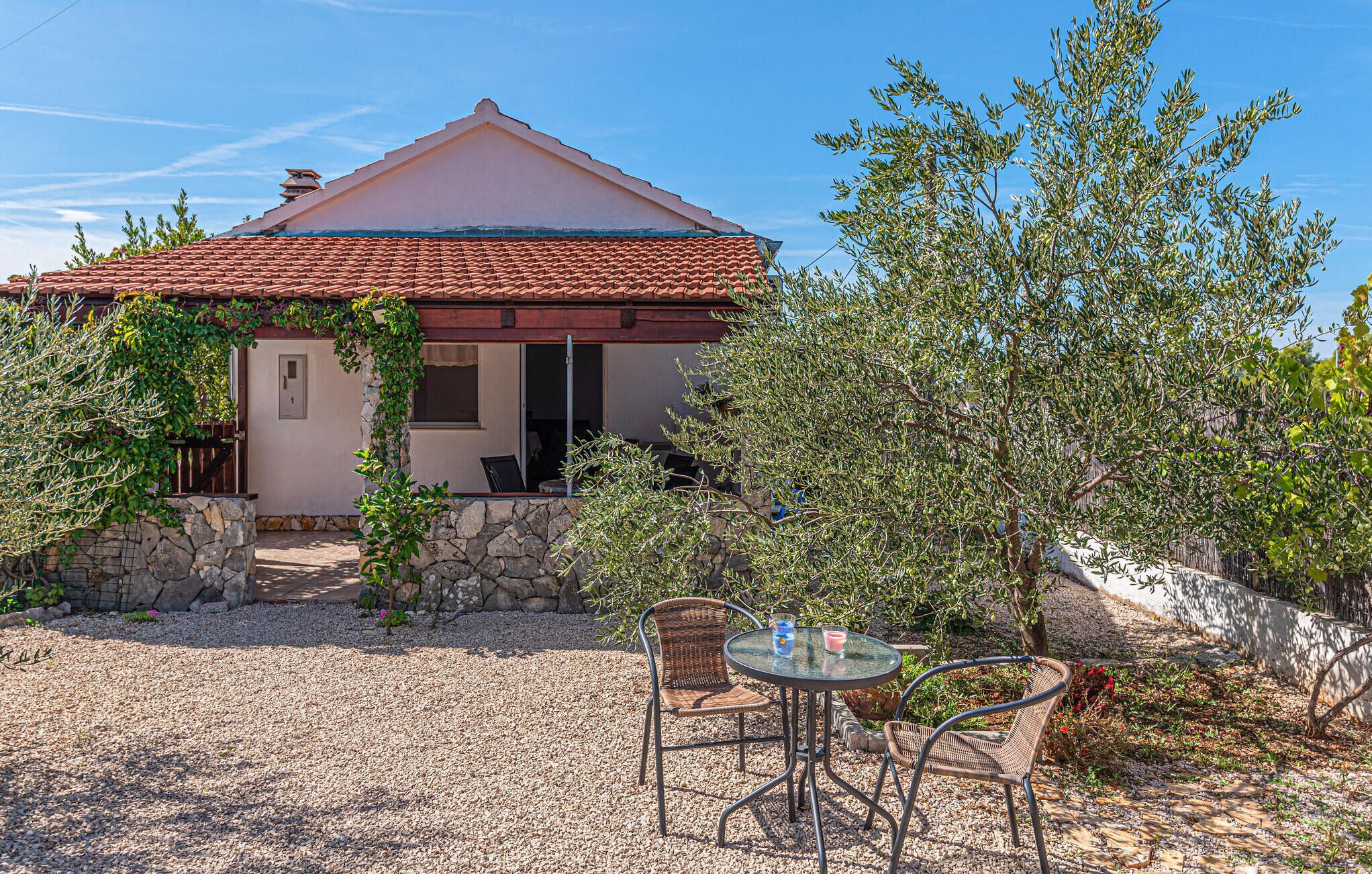 A house with a tiled roof, a stone wall, and a gravel patio with two wicker chairs and a table.