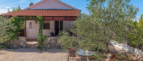 A house with a tiled roof, a stone wall, and a gravel patio with two wicker chairs and a table.