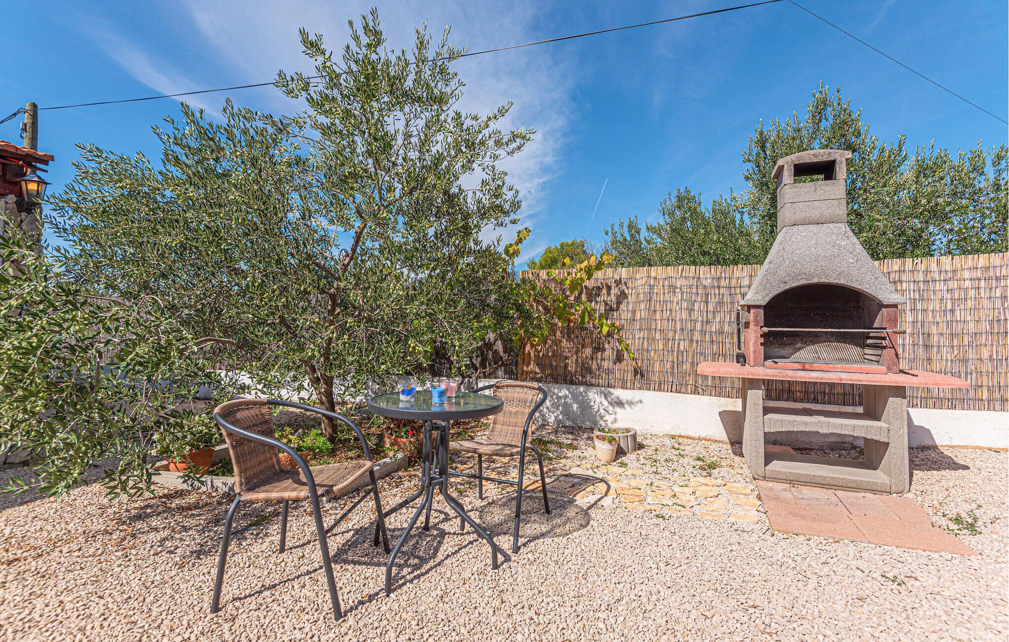 An outdoor patio with a stone pizza oven, wicker chairs, and a table.