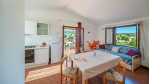 A cozy room with a dining table, chairs, a sofa with a colorful cushion, and a view of the outdoors. - 2 bedroom amazing apartment in San Teodoro OT (San Teodoro OT)