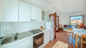 A compact kitchen with white cabinets, a gas stove, and a built-in oven. There is a dining area with a table and chairs, and a view of the outside through a window. - 2 bedroom amazing apartment in San Teodoro OT (San Teodoro OT)
