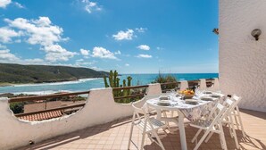 A terrace with a table set for dining, overlooking a coastal landscape with cacti and a view of the sea. - Stunning apartment in Porto Palma (Porto Palma)