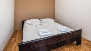 Ein kleines, ordentlich bezogenes Bett mit weißer Bettwäsche und Kissen, ein hölzernes Kopfstück und zwei gefaltete Handtücher auf dem Bett.