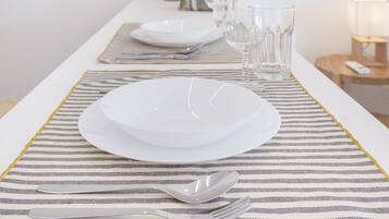 Een keurig gedekte eettafel met borden, bestek en glazen op een geruit placemat.