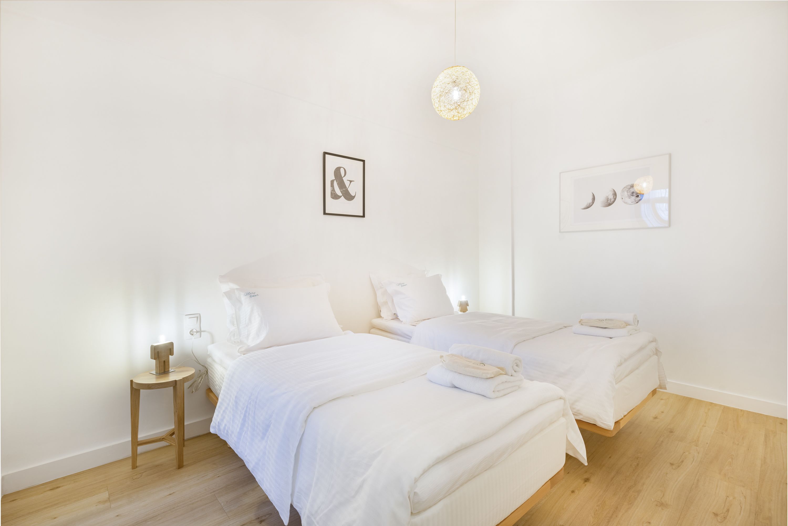 A minimalist hotel room with two beds, a bedside table, and a wall-mounted light fixture.