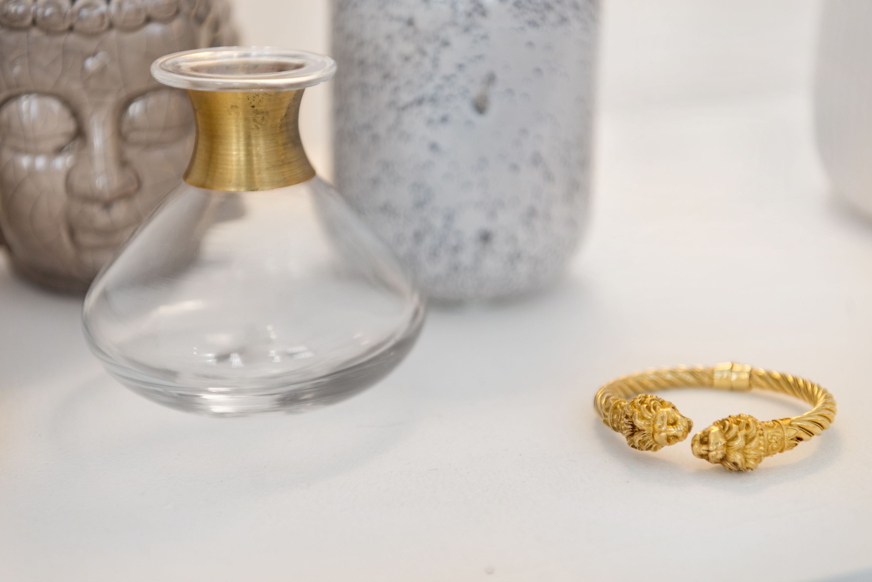A clear glass bottle and a gold bracelet with lion designs.