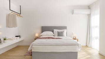 Une chambre à coucher au style minimaliste, comprenant un lit, des tables de chevet, un porte-serviettes mural et un appareil de climatisation.