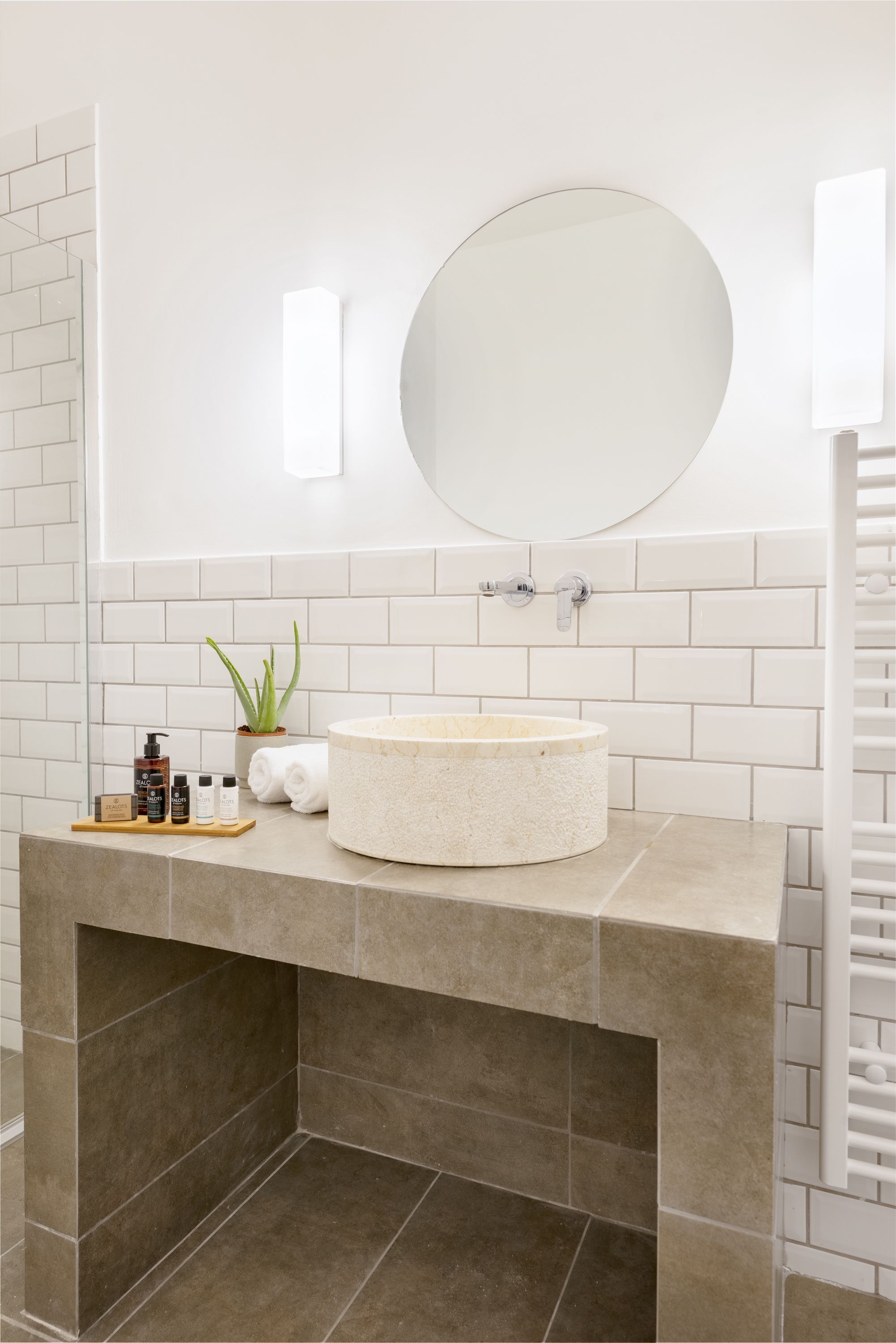 Une salle de bain avec un lavabo rond, des carreaux blancs, un miroir et un porte-serviettes.