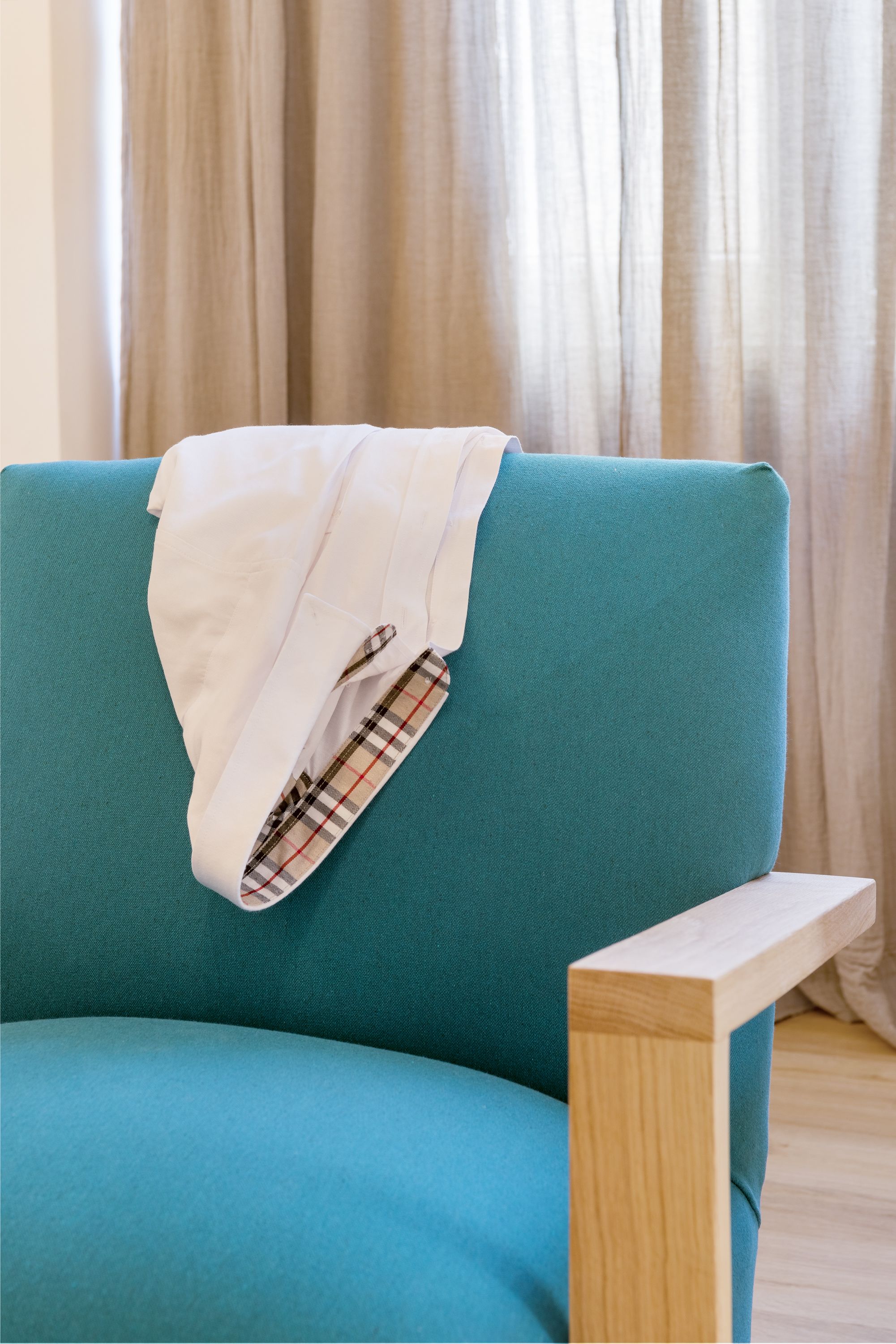A teal sofa with a plaid blanket and a white shirt draped over it.