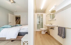 Relax in a serene bedroom with a comfortable bed, nightstand, and en-suite bathroom featuring a sink, mirror, and shower enclosure.