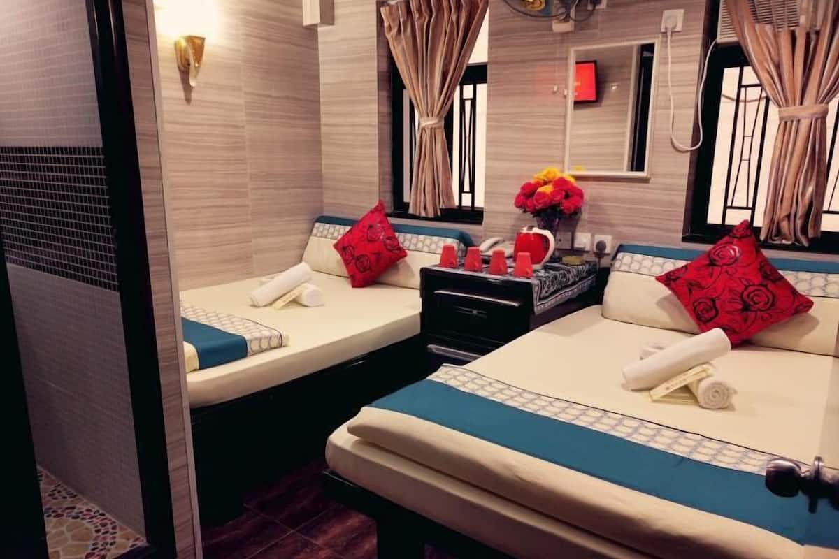 A hotel room with two beds, each with a blue and white bedspread, red floral pillows, and a small table with a vase of flowers.
