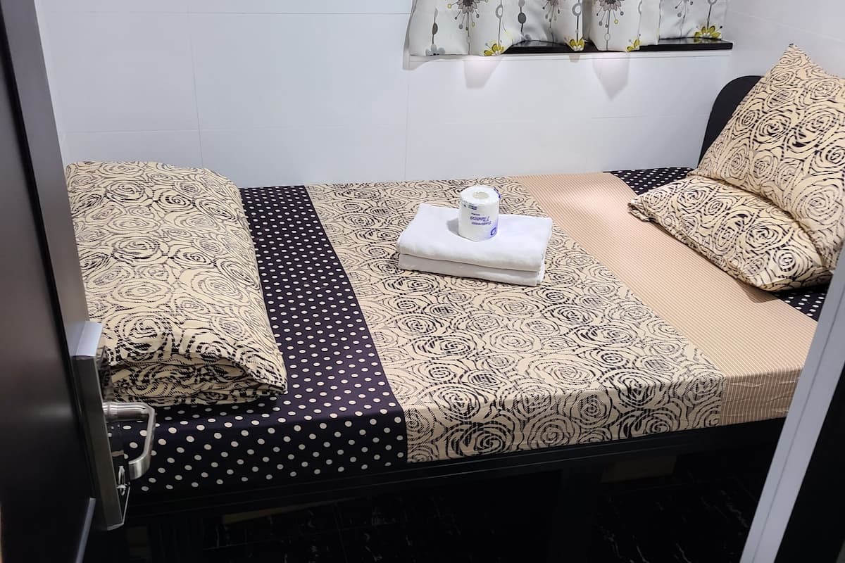 A small, neatly made bed with patterned bedding, a polka-dotted pillow, and a rolled towel.