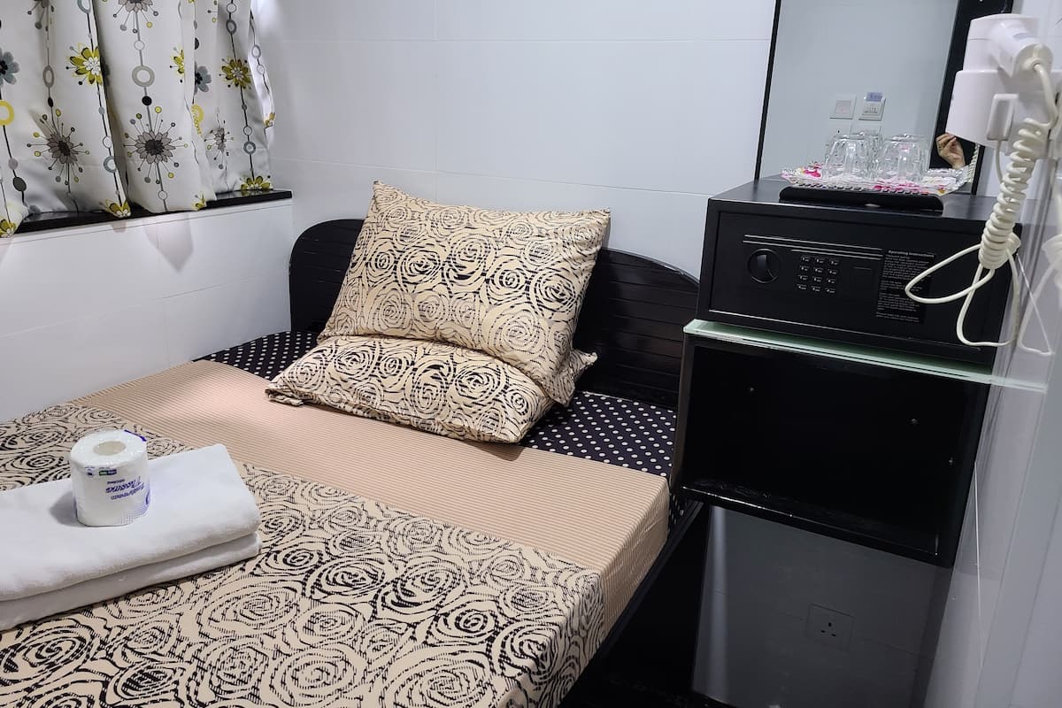 A hotel room with a bed, a pillow, a small table with a bottle, a microwave, and a telephone.