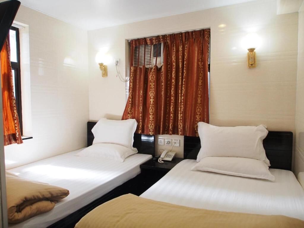 A hotel room with two single beds, a bedside table with a phone, and a window with curtains.
