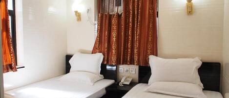 A hotel room with two single beds, a bedside table with a phone, and a window with curtains.